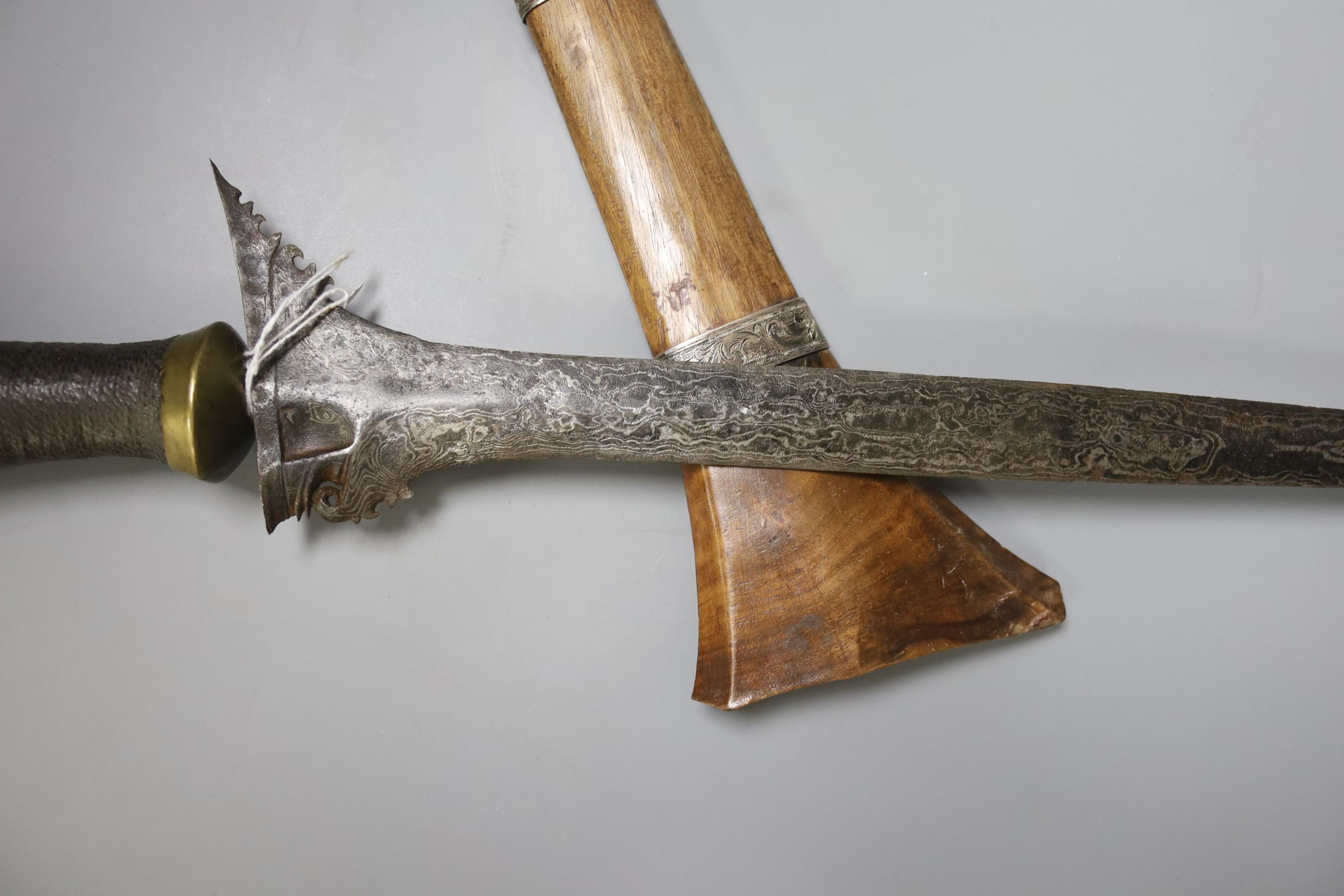 An Indonesian dagger kris, 19th century, earlier broad black and silver-coloured watered blade, brass mounted handle wound with woven hair, wooden scabbard with engraved silver mounts, blade 43.5cms